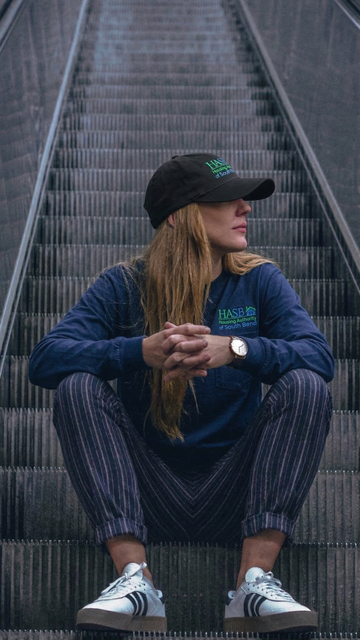 Person sitting on an escalator wearing a blue sweatshirt with visible branding.