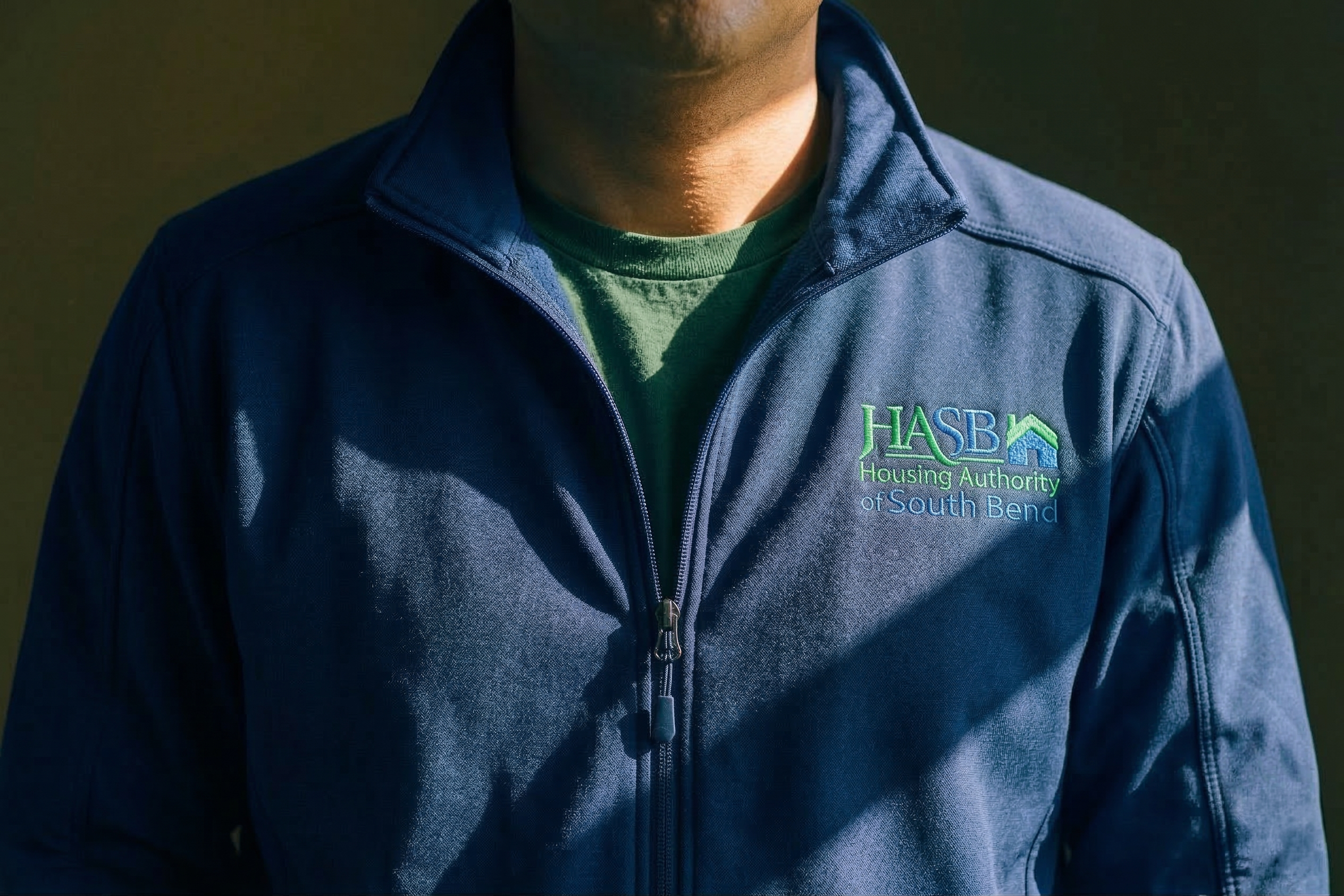 Person wearing a navy blue jacket with a logo on a dark background