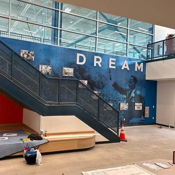 Modern indoor setting with a large 'DREAM' mural on a wall, featuring an escalator and various items on the floor.