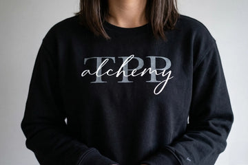 Person wearing a black sweatshirt with 'TPP alchemy' text on a plain background